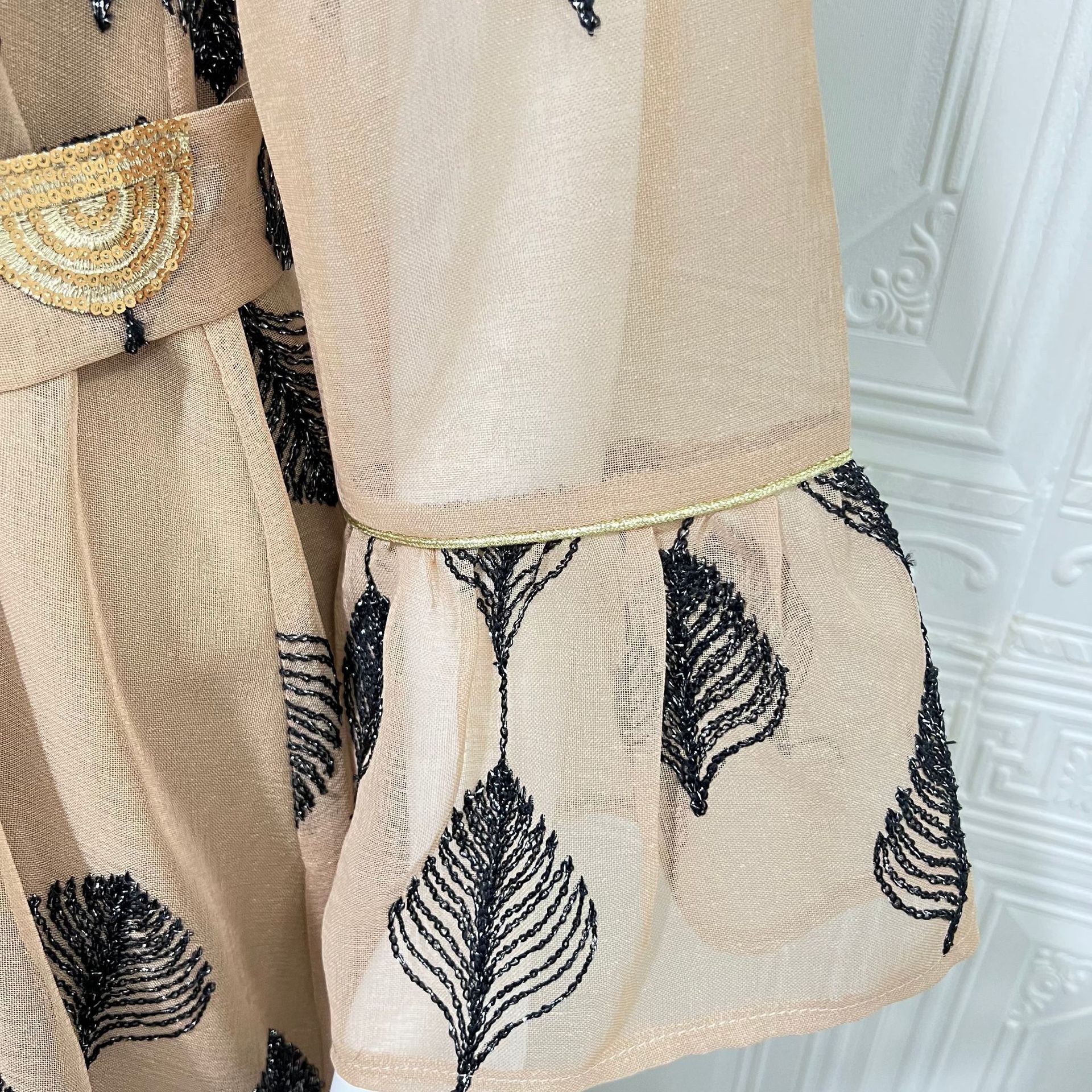 Desert FYP Viral Khaleeji Two-Piece Modest Co-ord Warm Sand Tone Light Woven Outer Kaftan Matching Solid Slip Dress All Over Vintage Black Leaf Print Handcrafted Golden Lace Trim Placket Elastic Gold Waist Belt Bell Flared Tiered Long Sleeve Ruffled